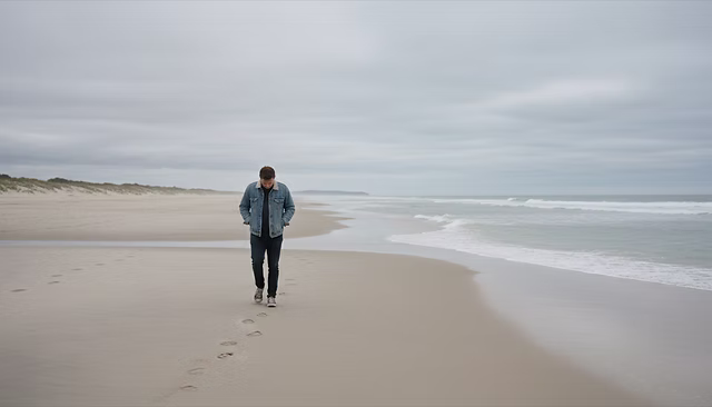 Medium shot view of a person walking alone along a sandy beach under a cloudy sky.